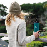 Woman standing on balcony holding Klean Kanteen TKWide insulated bottle with straw cap